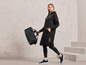 Une femme porte un sweat à capuche noir Jette Joop avec un legging et des baskets, et porte un sac de sport noir.