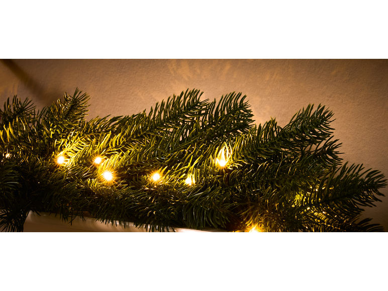 Gros plan d'une guirlande verte festive avec des lumières LED blanc chaud sur fond beige.