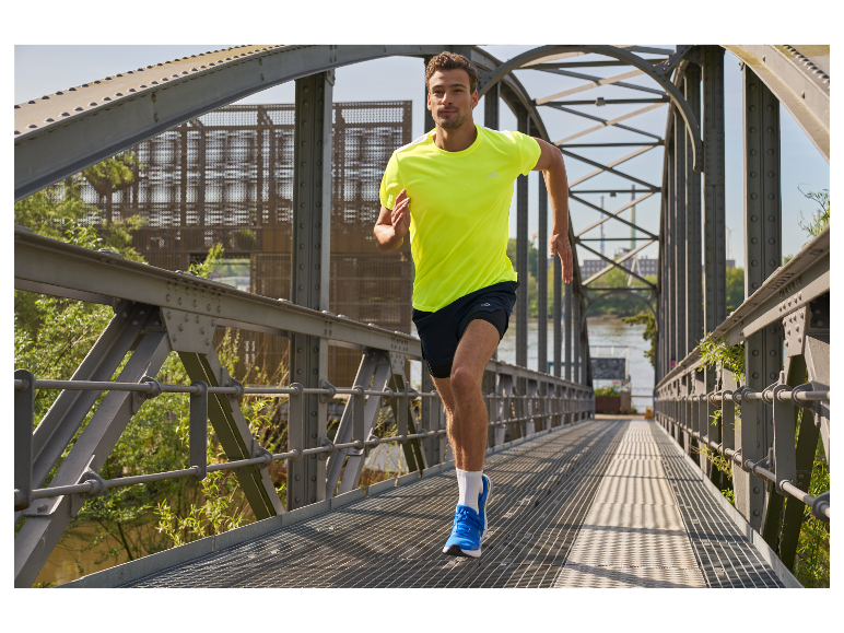 Un homme court sur un pont, vêtu d'un t-shirt jaune et de chaussures de course bleues.