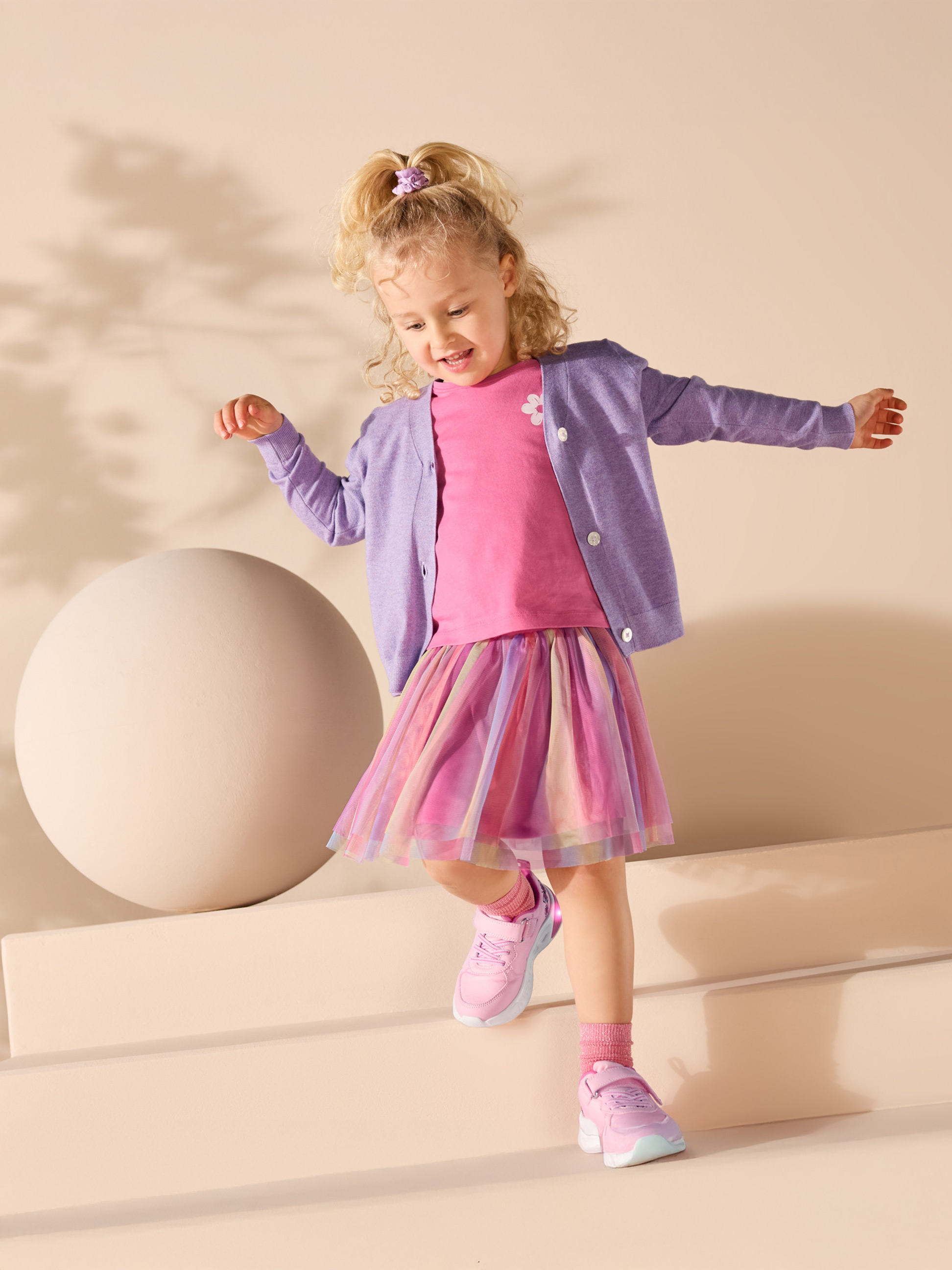 Fillette en t-shirt rose, cardigan violet et jupe en tulle colorée.
