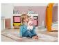 Petite fille jouant avec une poupée sur un tapis rose dans une chambre d'enfant.