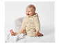 Un bébé heureux assis sur une couverture blanche portant une combinaison en peluche beige.