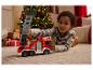 Enfant joue avec un camion de pompiers rouge sur le sol devant un sapin de Noël.