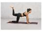 Femme en leggings noirs et soutien-gorge de sport faisant du yoga sur un tapis violet.