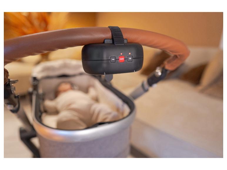 Un appareil ZAZU noir est attaché à la poignée marron d'une poussette avec un bébé.