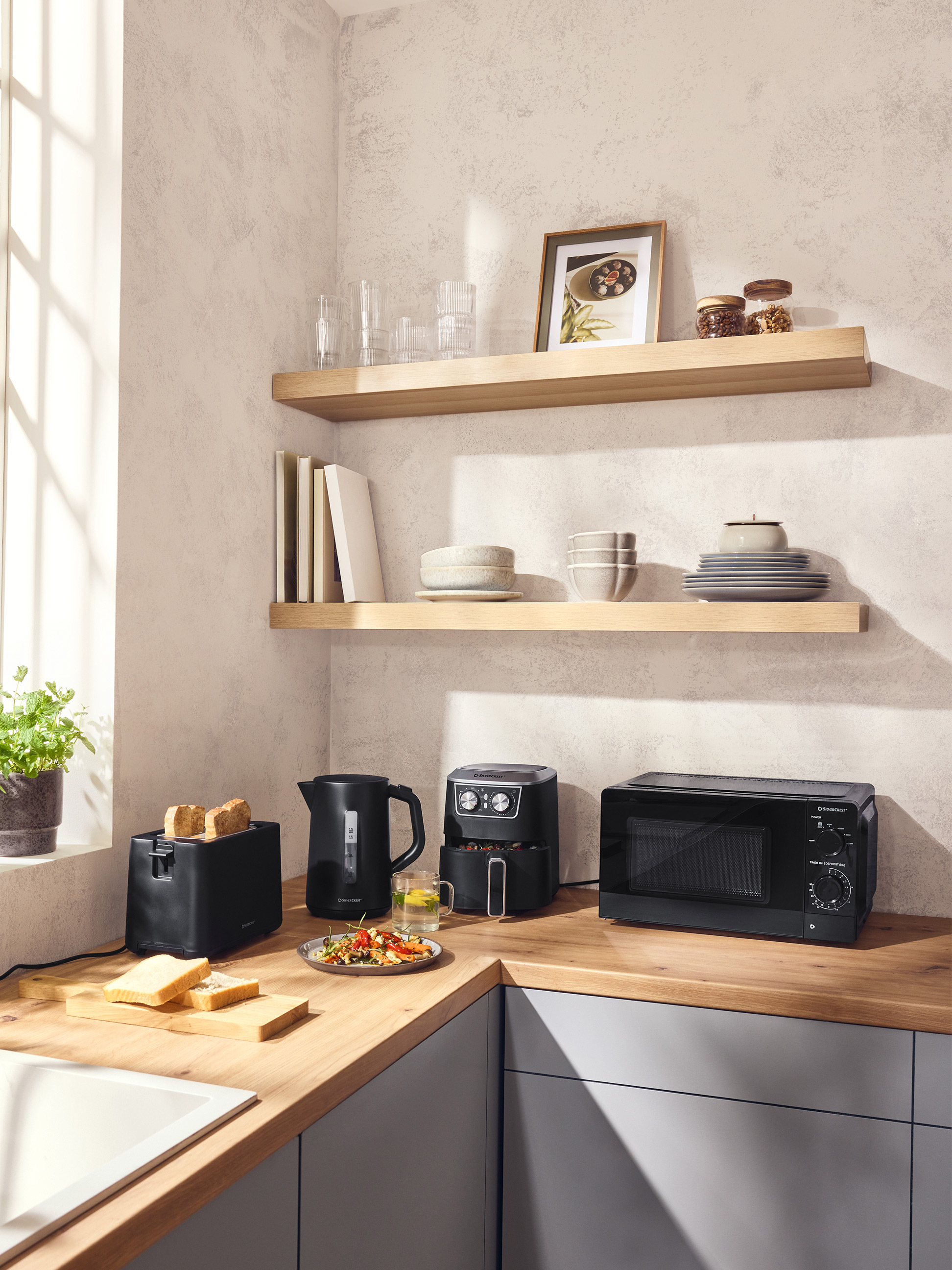 Cuisine moderne avec grille-pain, bouilloire, friteuse à air et micro-ondes noirs sur un comptoir en bois.