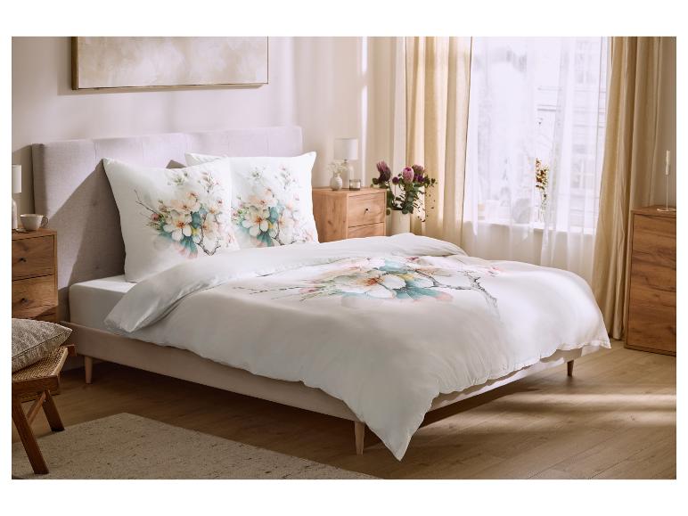 Chambre avec lit double, parure de lit blanche à motifs floraux et tables de chevet en bois.