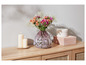 Des fleurs dans un vase en verre à pois sur une commode en bois avec deux bougies et deux boîtes.