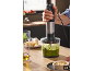 Un mixeur plongeant avec hachoir préparant un pesto vert sur un plan de travail.