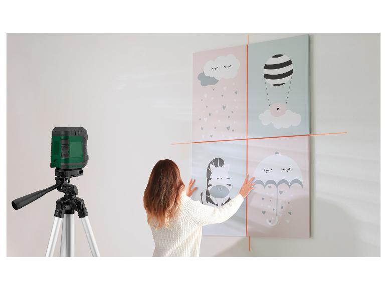 Femme utilisant un niveau laser pour accrocher des tableaux d'enfants au mur.