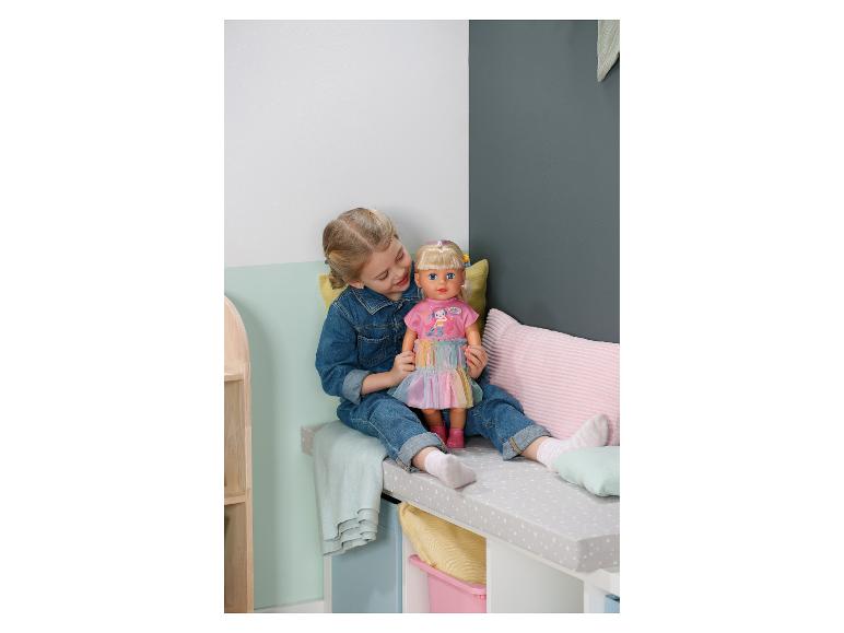 Fille en jean jouant avec une poupée en robe rose sur un banc.