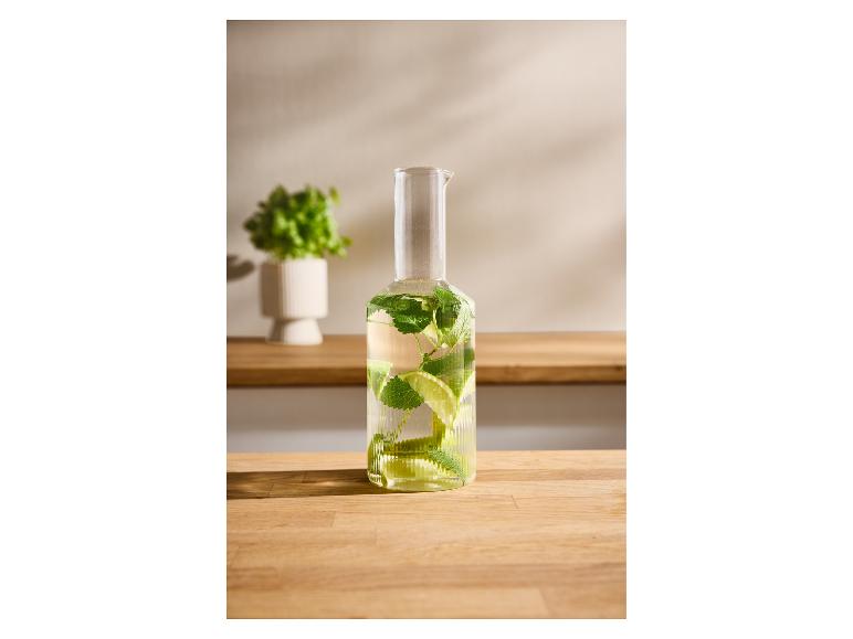 Bouteille en verre avec de l'eau, de la menthe et du citron vert sur une table en bois, avec une plante en arrière-plan.