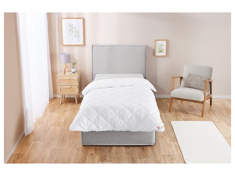 Une couette blanche matelassée sur un lit gris dans une chambre claire.