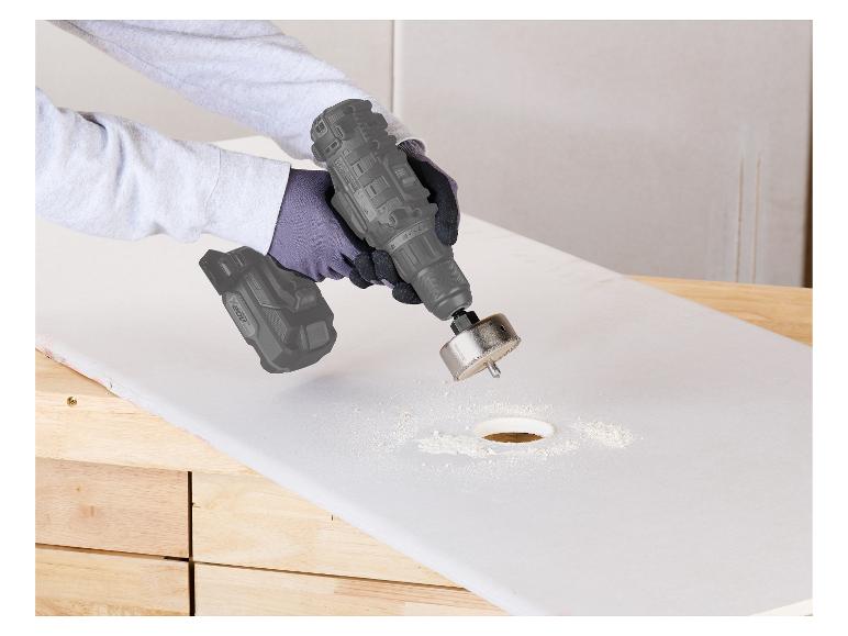 Une personne utilise une perceuse avec une scie cloche pour faire un trou dans une planche.