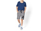 Un garçon porte un t-shirt bleu, un short gris à imprimé Jurassic World et des baskets bleues.