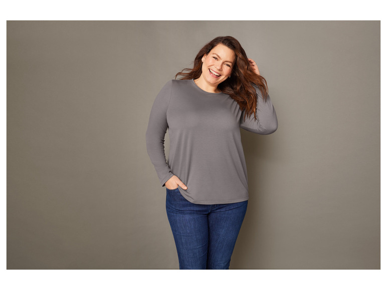 Une femme porte un t-shirt gris à manches longues et un jean bleu.