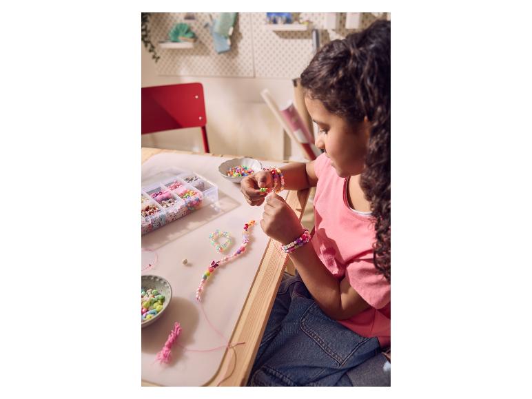 Enfant fabriquant des bracelets et colliers de perles colorés sur une table en bois.