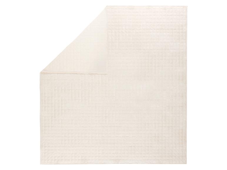 Couverture matelassée de couleur crème avec un motif carré, partiellement pliée.