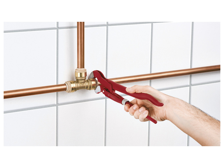 Un plombier utilise une clé à molette rouge Bahco sur des tuyaux en cuivre.