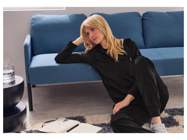 Femme en survêtement de velours noir assise par terre avec un carnet.