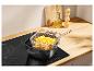 Friteuse avec frites sur une plaque à induction, avec huile et poivre en arrière-plan.