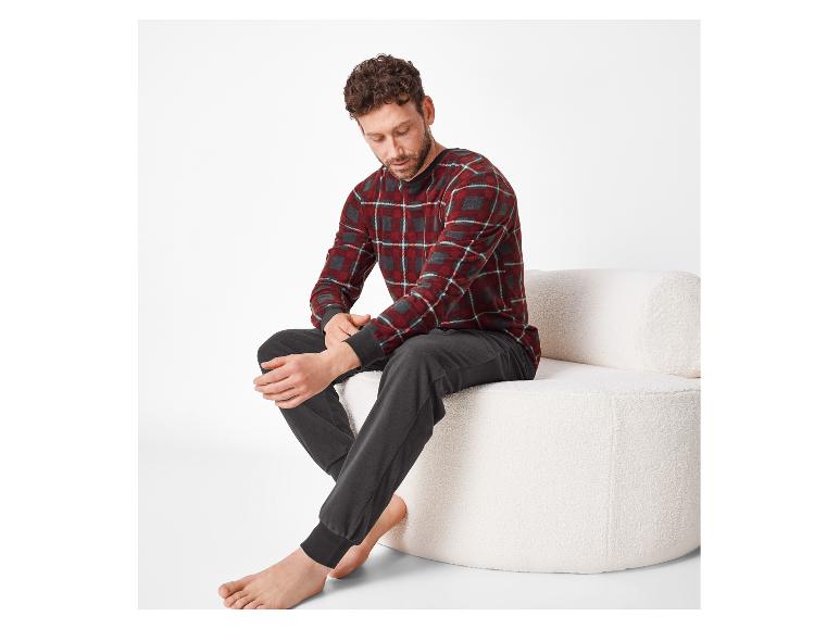 Homme en pyjama à carreaux rouges et pantalon gris, assis sur un canapé blanc.