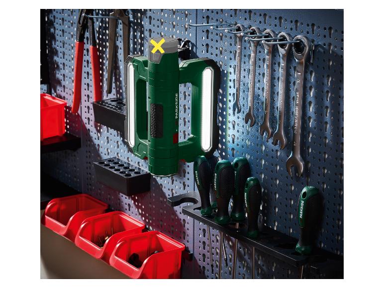 Lampe de travail verte et outils suspendus sur un panneau perforé.