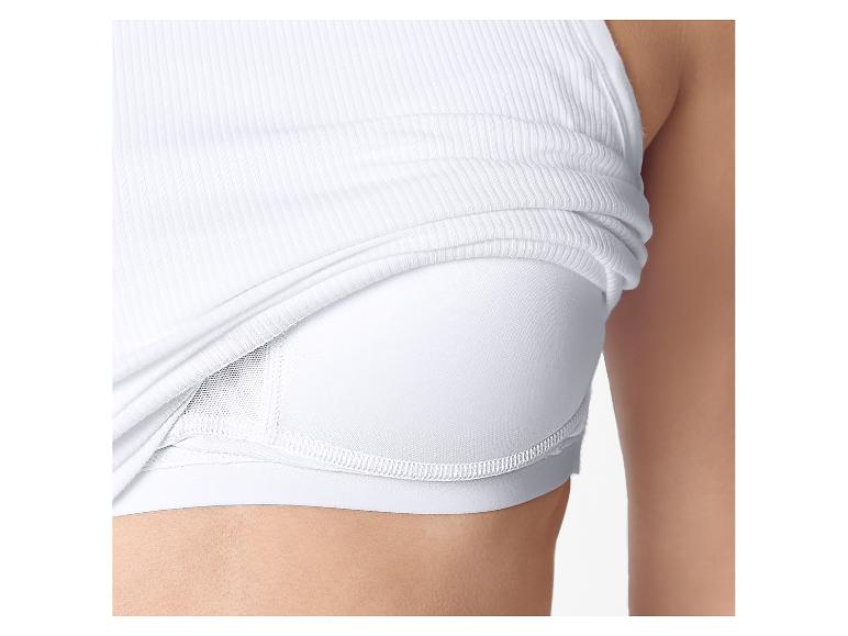 Gros plan d'une femme portant un débardeur blanc côtelé sur une brassière de sport blanche.