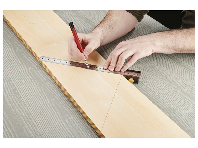 Une personne utilise une règle et un crayon pour tracer une ligne sur un morceau de bois.