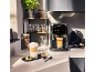 Machine à café avec deux tasses de café, des grains de café et une plante dans la cuisine.