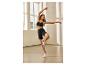 Femme en brassière de sport noire et short cycliste posant dans un studio de danse.
