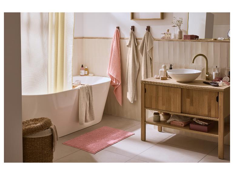 Salle de bain avec baignoire blanche, meuble vasque en bois et tapis de bain rose.