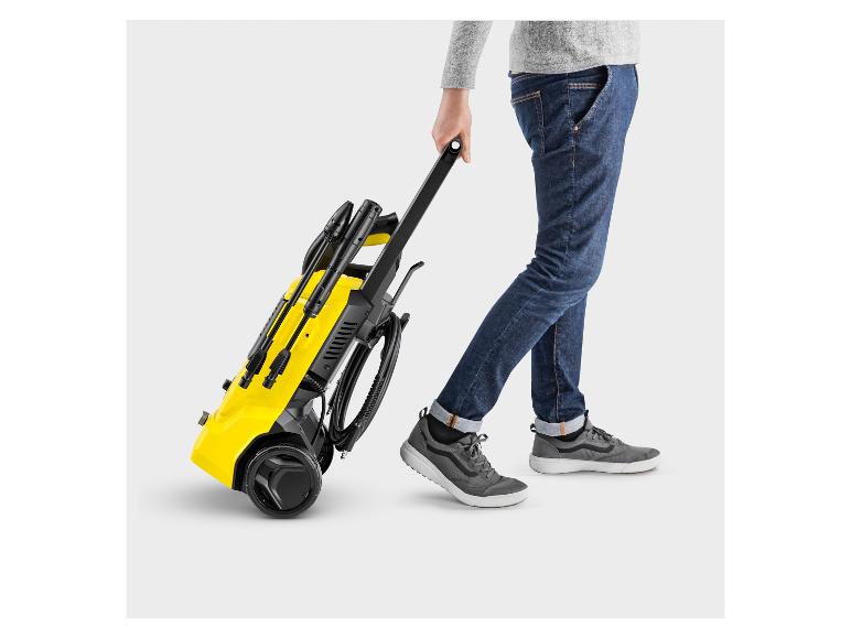 Personne tirant un nettoyeur haute pression Kärcher jaune avec accessoires.