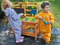 Deux enfants en imperméables jouent avec une cuisine en bois pour enfants.