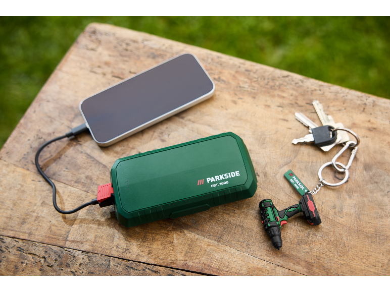 Batterie externe verte chargeant un smartphone, avec des clés et un porte-clés mini-perceuse.