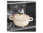 Cocotte en fonte couleur crème avec un bouton doré à l'intérieur d'un four sur une grille.
