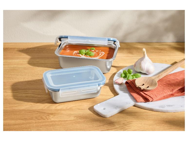Boîtes alimentaires en acier inoxydable avec soupe de tomates, ail et basilic sur une surface en bois.