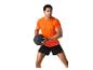 Un homme en t-shirt orange et short noir tient un ballon de médecine.