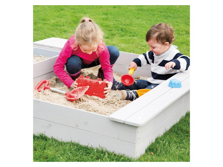 Deux enfants jouent dans un bac à sable en bois.