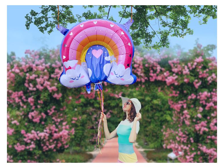 Femme avec un chapeau et un ballon arc-en-ciel dans un jardin de roses.