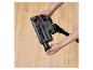 Mains tenant un accessoire d'aspirateur avec brosse visible sur un parquet en bois.