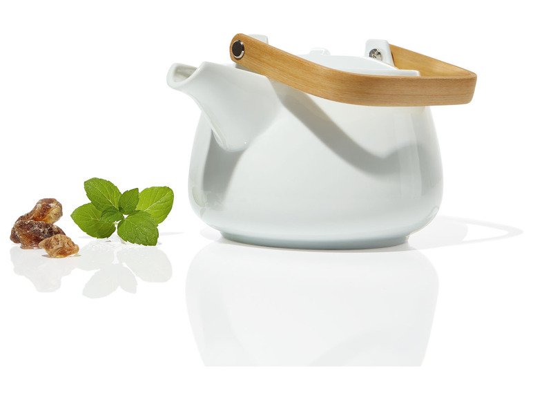 Théière blanche avec une poignée en bois, des morceaux de sucre et de la menthe.