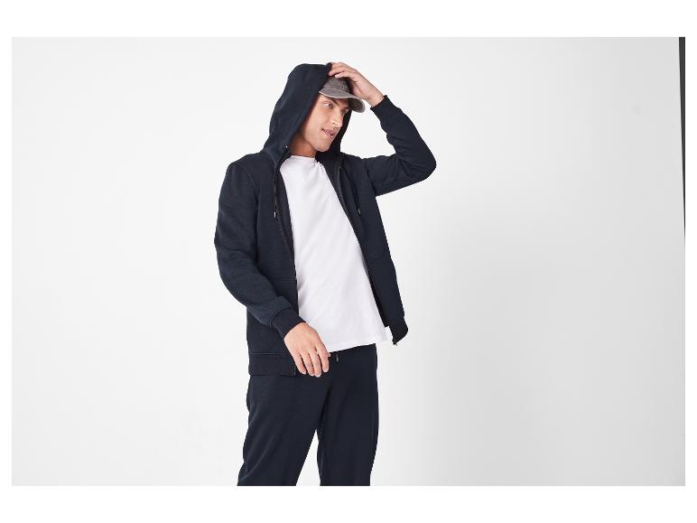 Homme en sweat à capuche bleu foncé, T-shirt blanc et pantalon de survêtement assorti.