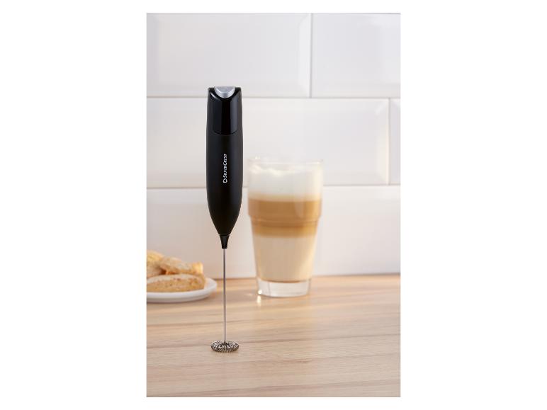 Mousseur à lait noir sur une surface en bois à côté d'un verre de latte et de biscuits