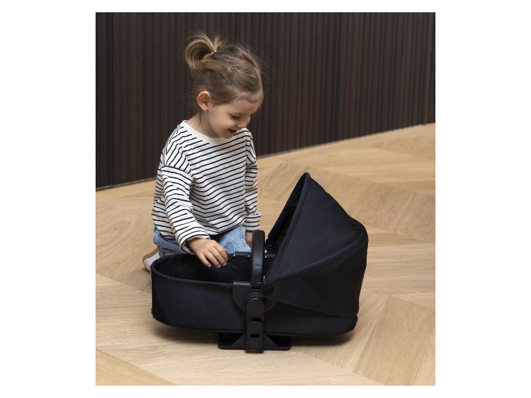 Un enfant joue avec une nacelle de poussette noire.
