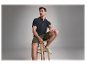 Un homme pose en polo noir et short kaki.