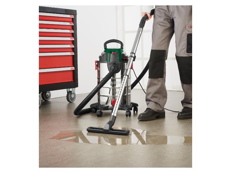 Un homme nettoie une flaque d'eau avec un aspirateur eau et poussière près d'une armoire à outils.