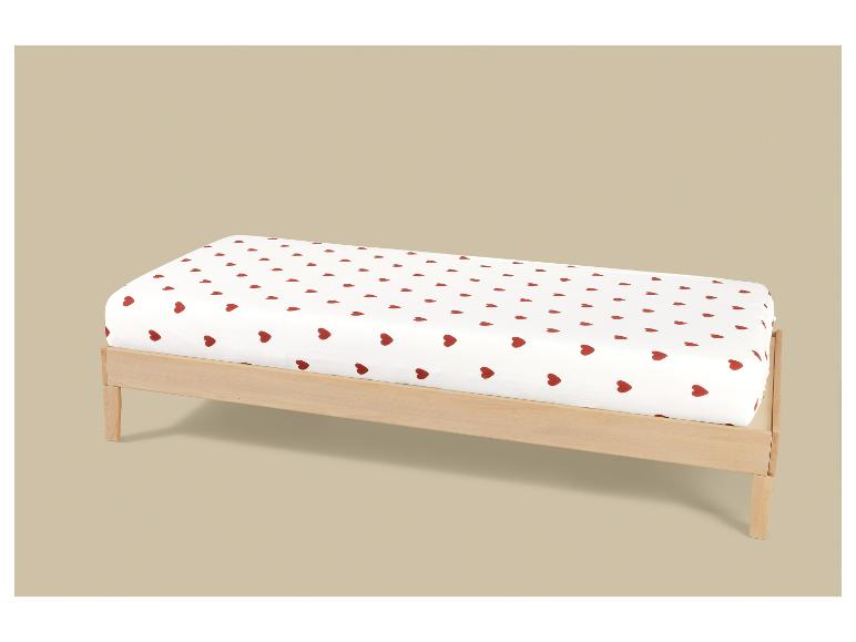 Lit d'enfant avec un drap-housse blanc à cœurs rouges.