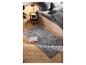 Tapis gris à motif géométrique dans une chambre avec parquet et lit.