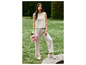 Une femme en haut et pantalon beiges, avec des fleurs et des baskets blanches dans un jardin.